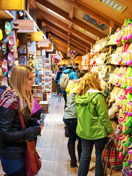 Visitors browsing colorful wooden clogs at a shop in Zaanse Schans, Netherlands.