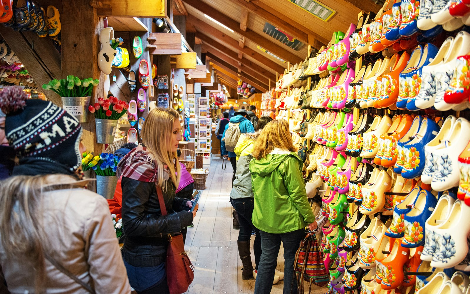 Visitors browsing colorful wooden clogs at a shop in Zaanse Schans, Netherlands.