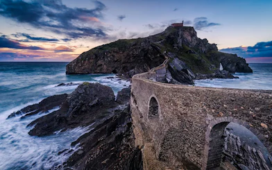 Stone bridge leading to Gaztelugatxe islet at sunset, part of Biscay Bridge tour from Bilbao.