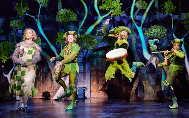 Performers in medieval costumes on stage during a Spamalot musical scene.