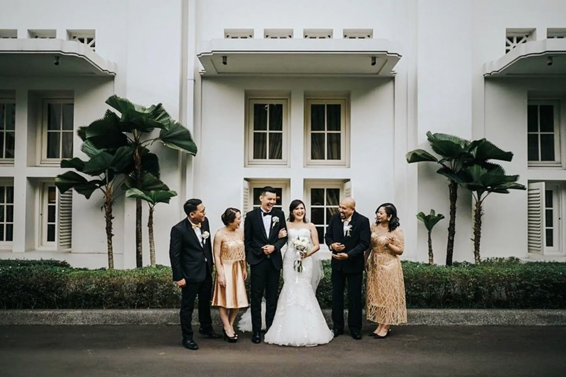 Wedding party posing outside a white building in Jakarta during a professional photoshoot by Viufinder.
