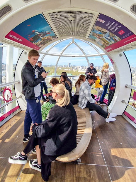 Visitors inside a London Eye capsule with city views in the background.