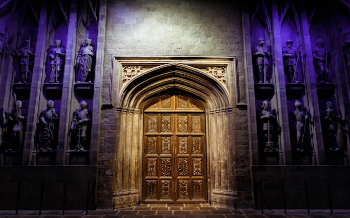 Great Hall entrance at Harry Potter™ Warner Bros. Studio Tour, featuring ornate wooden doors and knight statues.