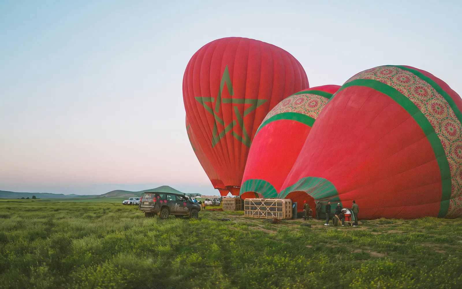 Hot air balloons preparing for sunrise flight in Marrakesh field.