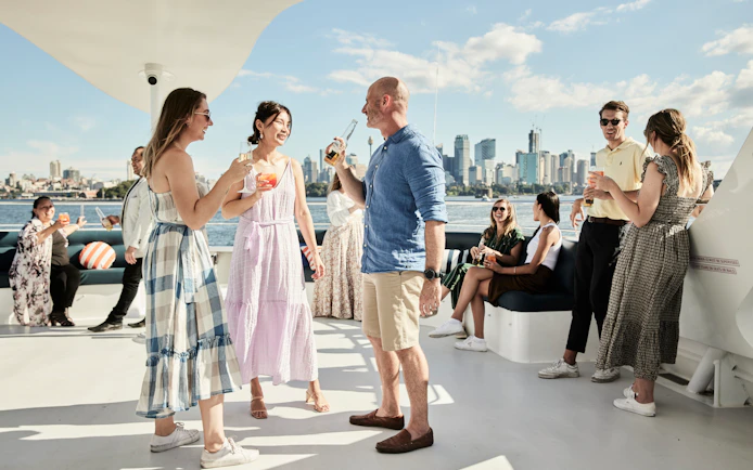 Guests enjoying drinks on a Sydney Harbour dinner cruise with city skyline in the background.