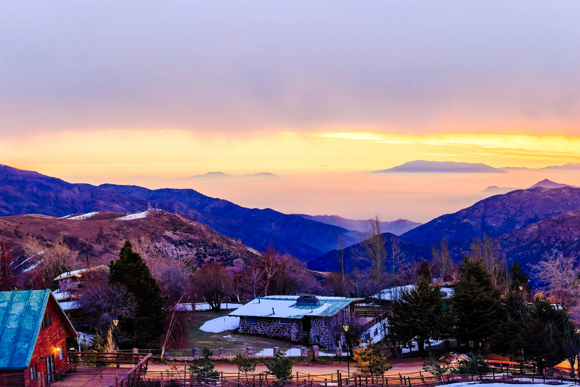Sunset over the Andes Mountains near Santiago with rustic cabins in the foreground.