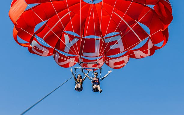 Parasailing over Albufeira with a red parachute against a clear blue sky.