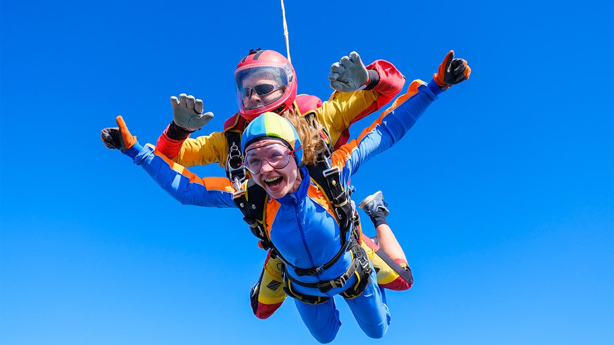 Tandem skydivers freefalling over Abu Dhabi with clear blue sky.