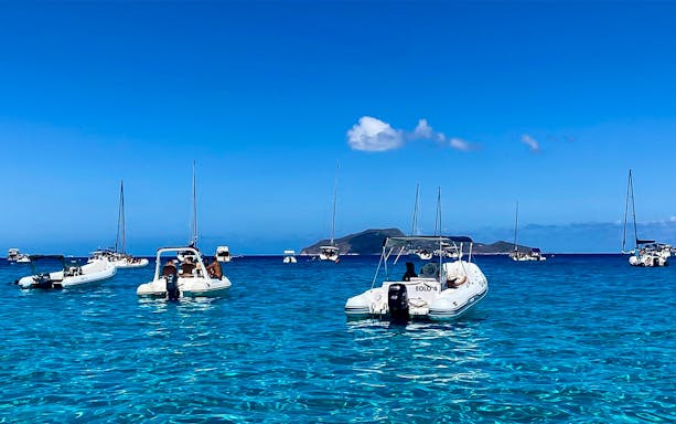 Boats anchored in clear blue waters near Favignana, Italy, with distant islands visible.