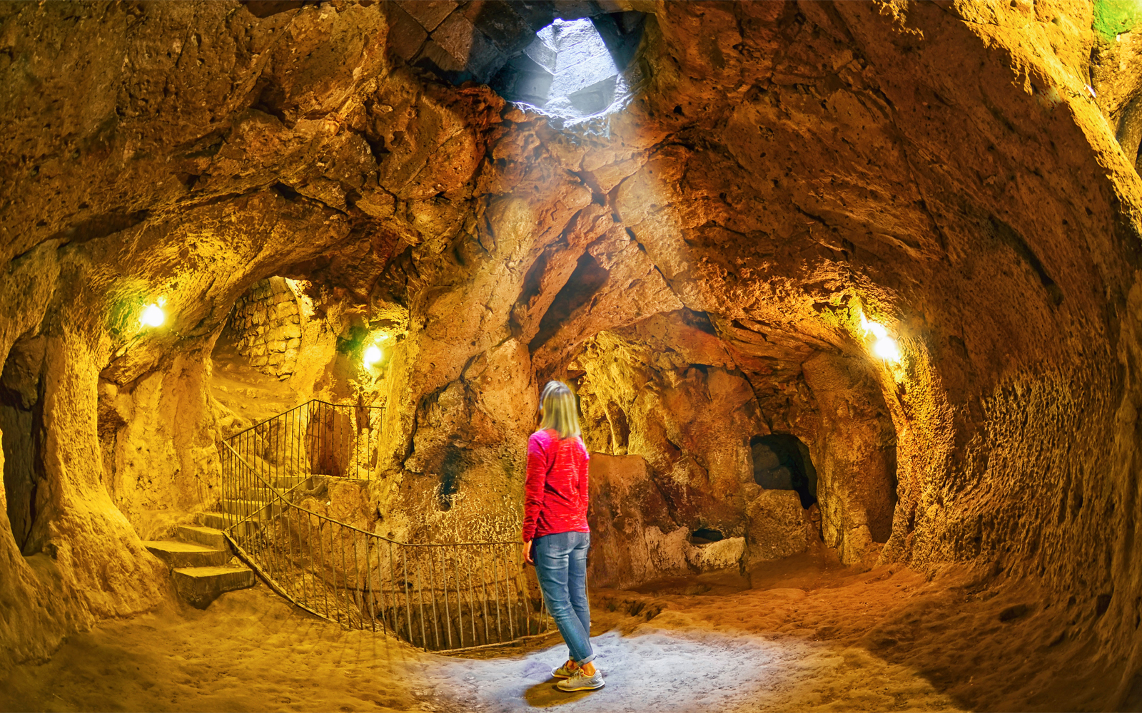 Visitor exploring Derinkuyu underground city cave with stone walls and stairway.