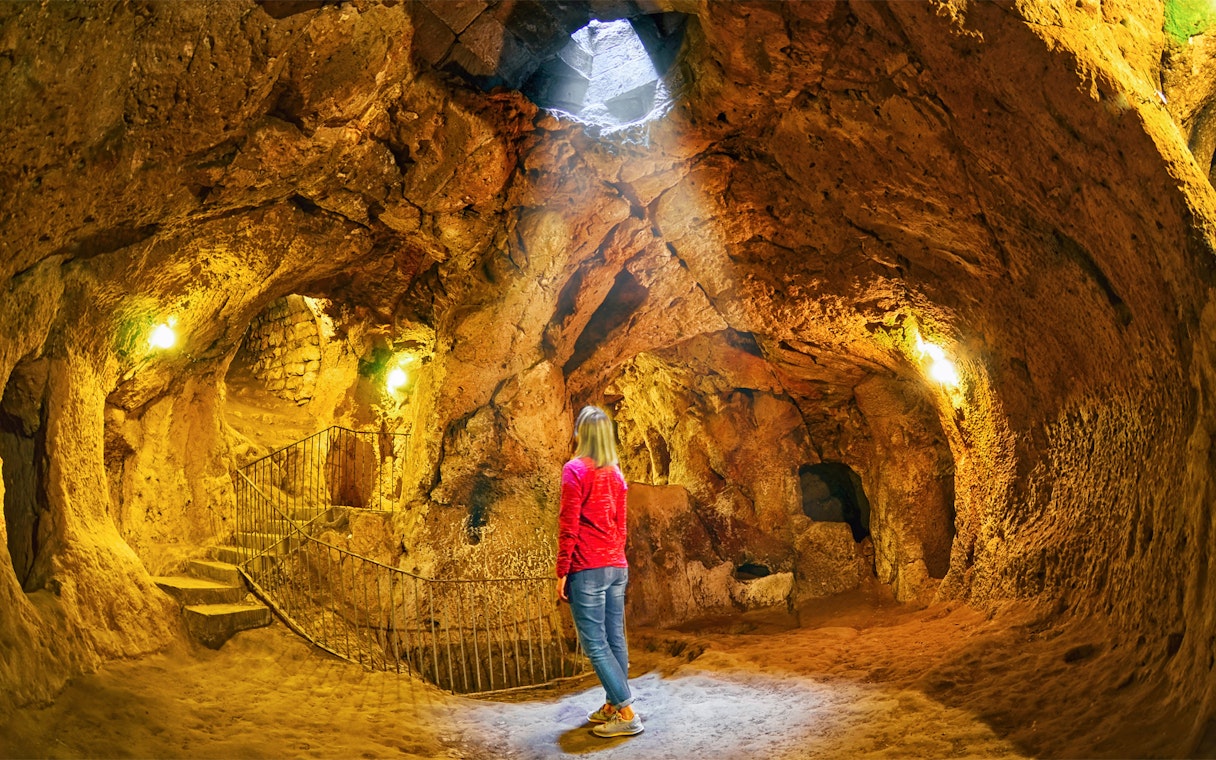 Visitor exploring Derinkuyu underground city cave with stone walls and stairway.