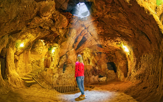 Visitor exploring Derinkuyu underground city cave with stone walls and stairway.