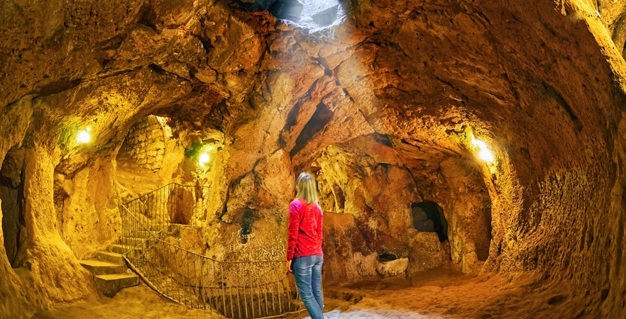 Visitor exploring Derinkuyu underground city cave with stone walls and stairway.