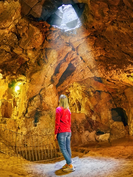 Visitor exploring Derinkuyu underground city cave with stone walls and stairway.