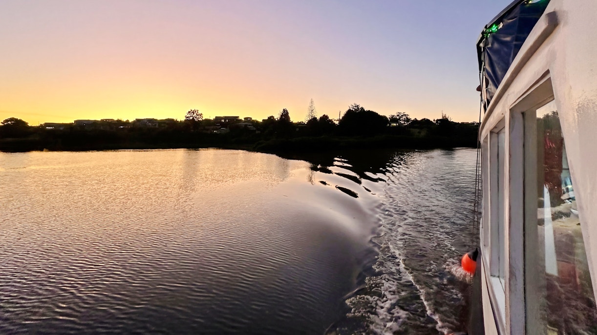 Boat cruising at sunset towards Riverhead Tavern on scenic river.