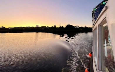 Boat cruising at sunset towards Riverhead Tavern on scenic river.
