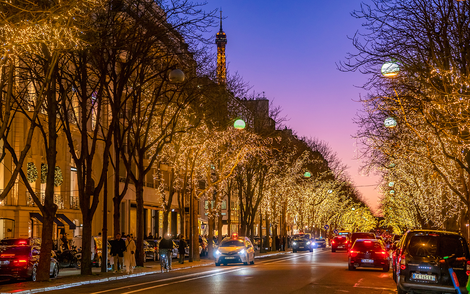 Avenue Montaigne in Paris adorned with Christmas lights, Eiffel Tower in the background.