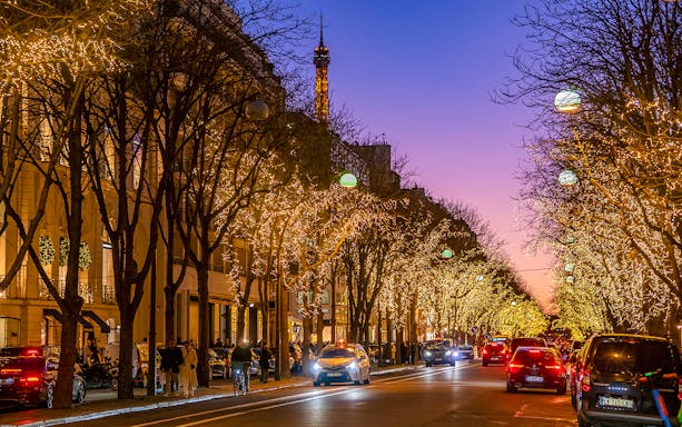 Avenue Montaigne in Paris adorned with Christmas lights, Eiffel Tower in the background.