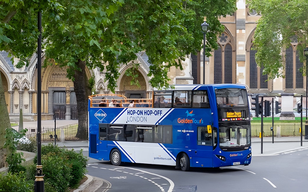 Open-top London hop-on hop-off bus near historic building.