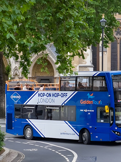 Open-top London hop-on hop-off bus near historic building.