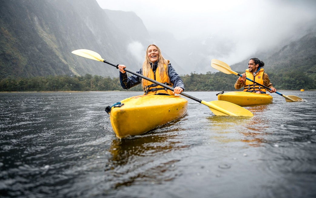 Couple kayaking in Milford Sound with misty mountains in the background.
