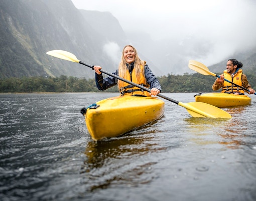 Couple kayaking in Milford Sound with misty mountains in the background.