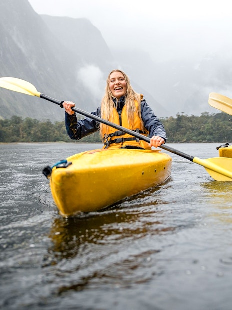 Couple kayaking in Milford Sound with misty mountains in the background.
