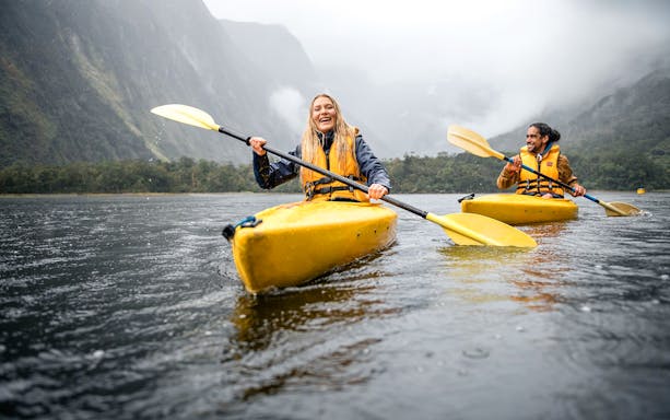 Couple kayaking in Milford Sound with misty mountains in the background.