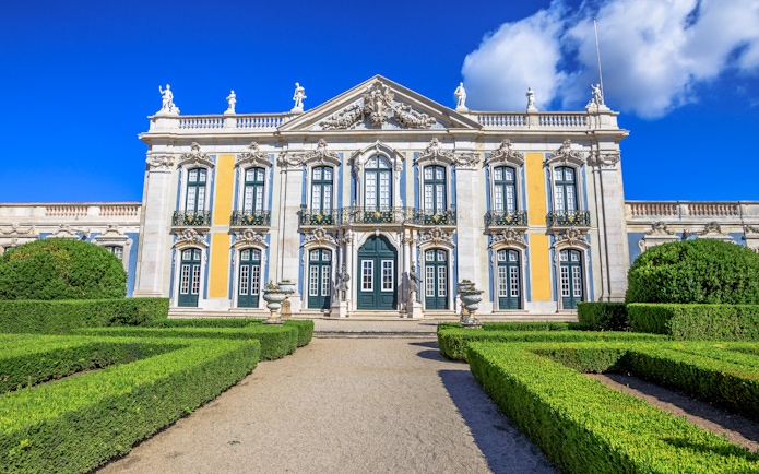 Facade of Queluz National Palace with ornate windows and manicured gardens.
