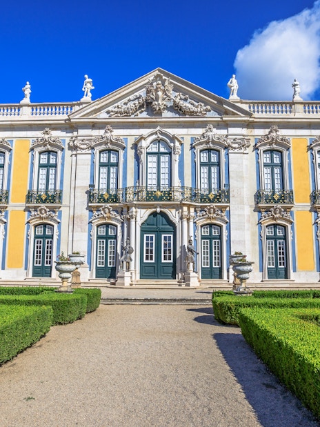 Facade of Queluz National Palace with ornate windows and manicured gardens.