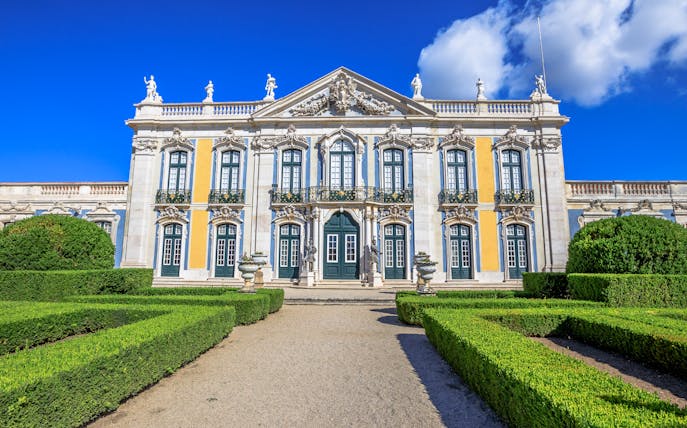 Facade of Queluz National Palace with ornate windows and manicured gardens.