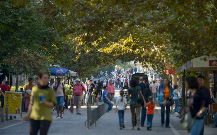 Crowded pedestrian street in Plaka, Athens, with people walking under tree-lined paths.