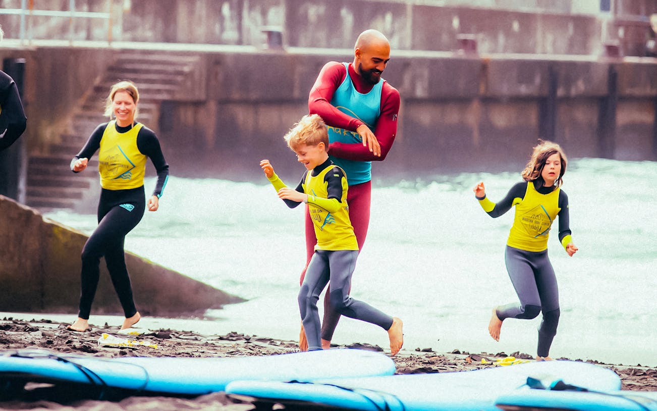 Family learning to surf on a beach with instructor guiding children.
