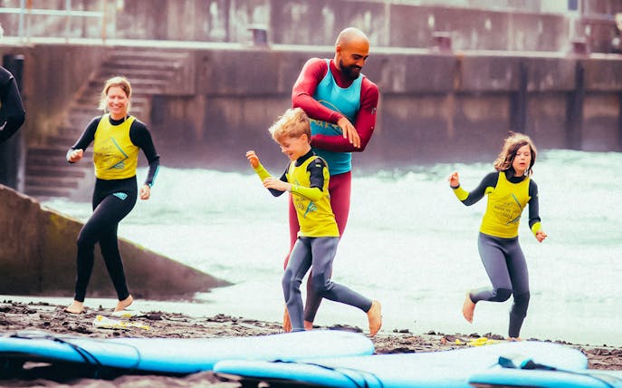 Family learning to surf on a beach with instructor guiding children.