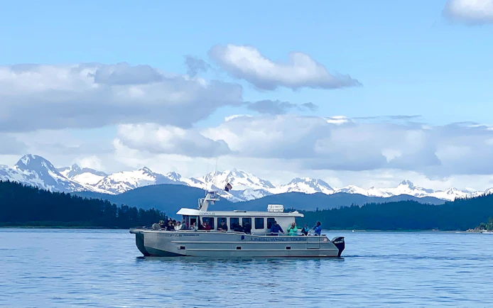 Catamaran on Juneau whale watching tour with snowy mountains in the background.