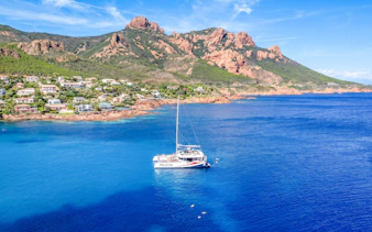 Catamaran sailing in Villefranche bay with coastal view and mountains in the background.