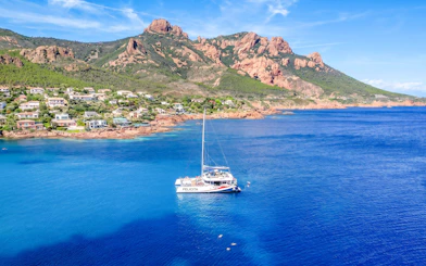 Catamaran sailing in Villefranche bay with coastal view and mountains in the background.