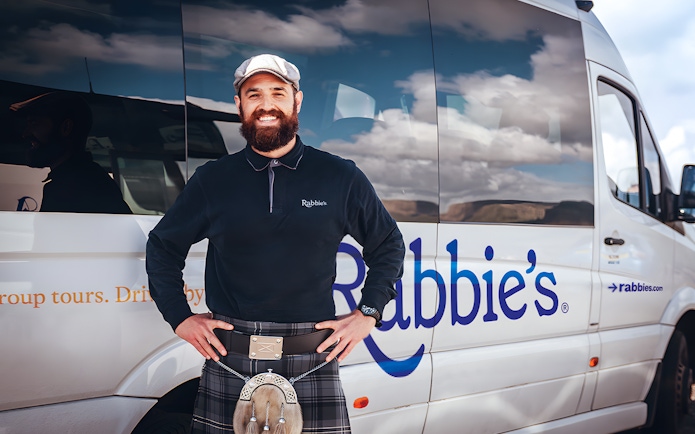 Tour guide standing beside Rabbie's tour vehicle for day trip.