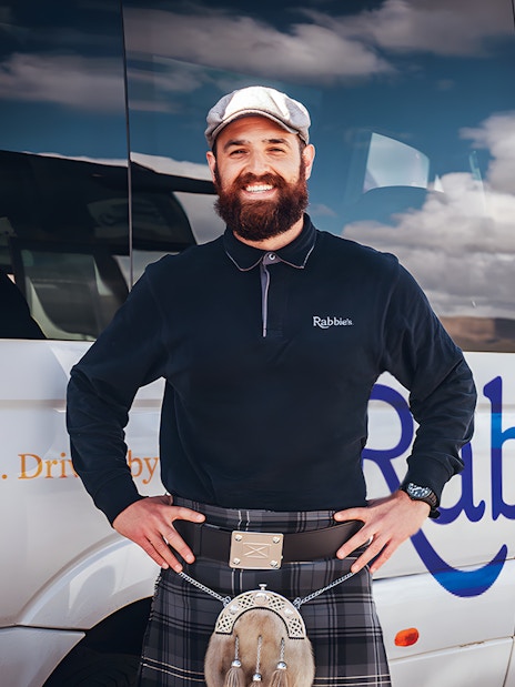 Tour guide standing beside Rabbie's tour vehicle for day trip.