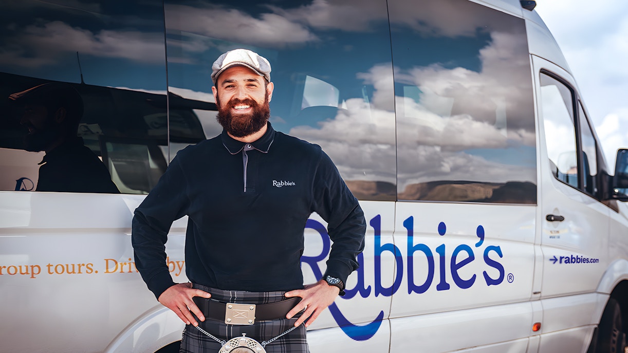Tour guide standing beside Rabbie's tour vehicle for day trip.