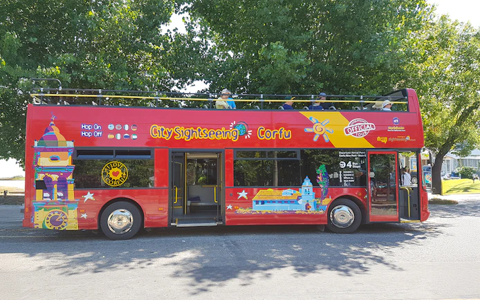 City Sightseeing hop on hop off tour bus in Corfu parked under trees.