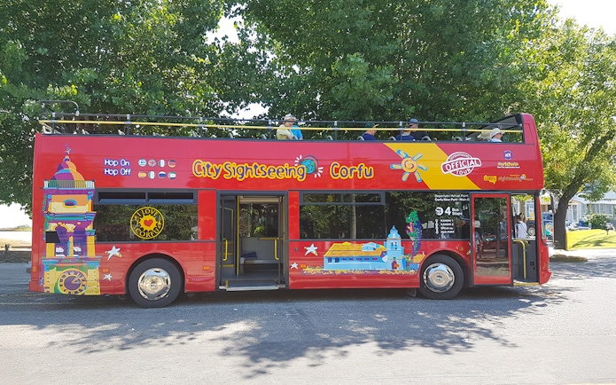 City Sightseeing hop on hop off tour bus in Corfu parked under trees.
