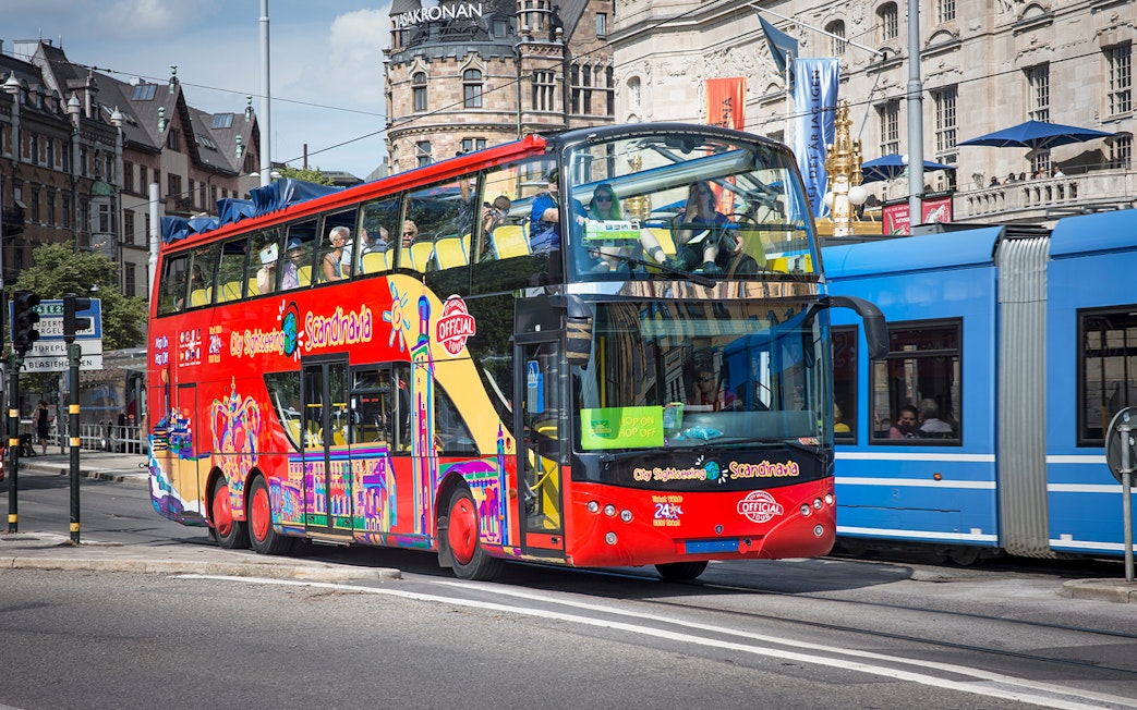 Red double-decker bus on Stockholm Hop-On-Hop-Off Tour passing historic buildings.