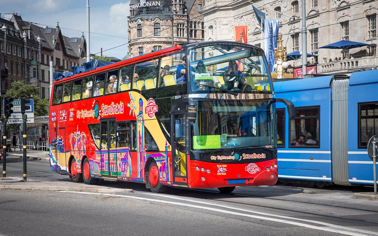 Red double-decker bus on Stockholm Hop-On-Hop-Off Tour passing historic buildings.