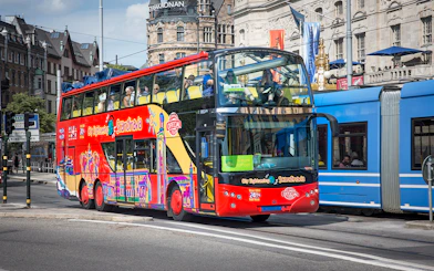 Red double-decker bus on Stockholm Hop-On-Hop-Off Tour passing historic buildings.
