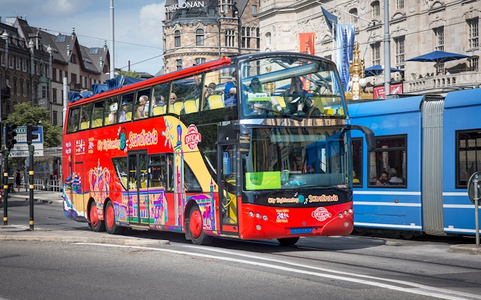 Red double-decker bus on Stockholm Hop-On-Hop-Off Tour passing historic buildings.