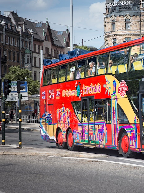 Red double-decker bus on Stockholm Hop-On-Hop-Off Tour passing historic buildings.
