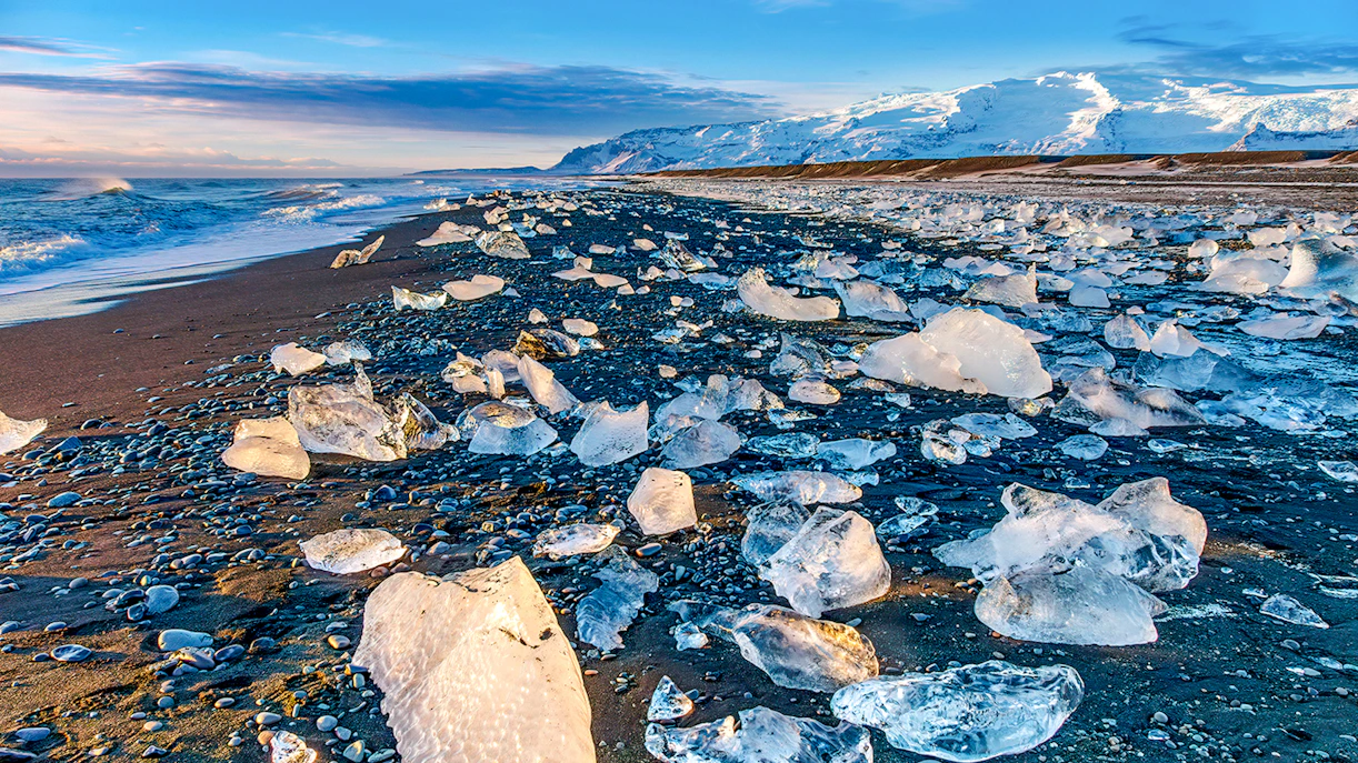 Ice chunks on Black Diamond Beach, Fellsfjara, Iceland with ocean and snowy mountains in the background.