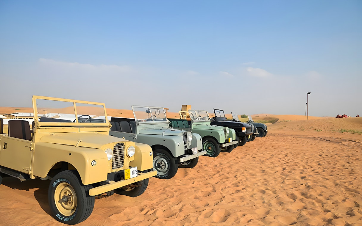 Vintage Land Rovers lined up in the desert for a hot air balloon experience.