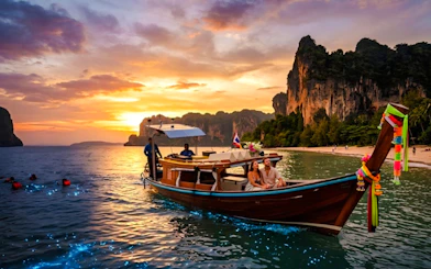 Longtail boat at sunset with tourists enjoying bioluminescent waters near Railay Beach, Krabi.